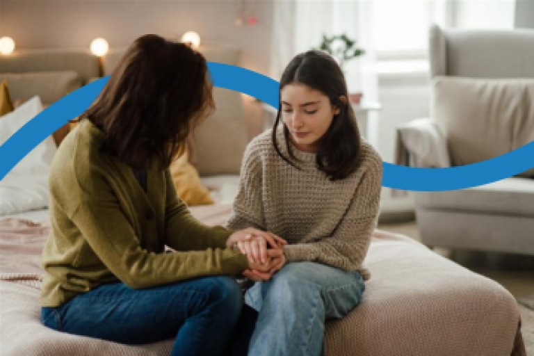 A female foster carer sits on a bed and talks with a teenage girl.