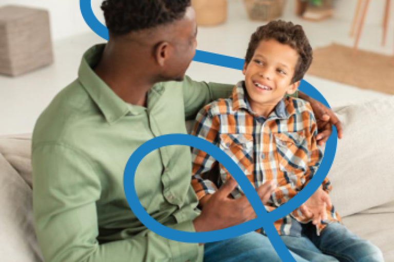 A male foster carer and a teenage boy sit on a sofa talking.
