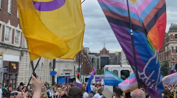 Flags and people marching in the city centre during Leeds Pride 2024.