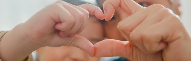 a child and an adult forming a heart shape by pressing together their fingers