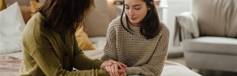 A female foster carer sits on a bed and talks with a teenage girl.