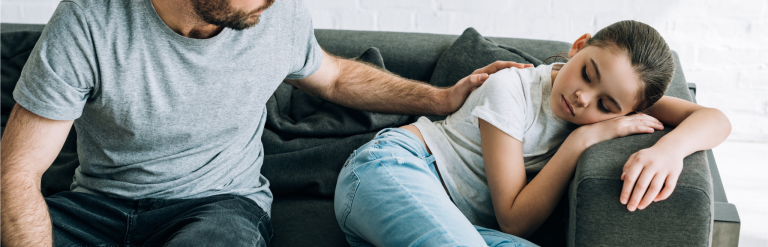 A male foster carer comforts a young girl sitting on a sofa.
