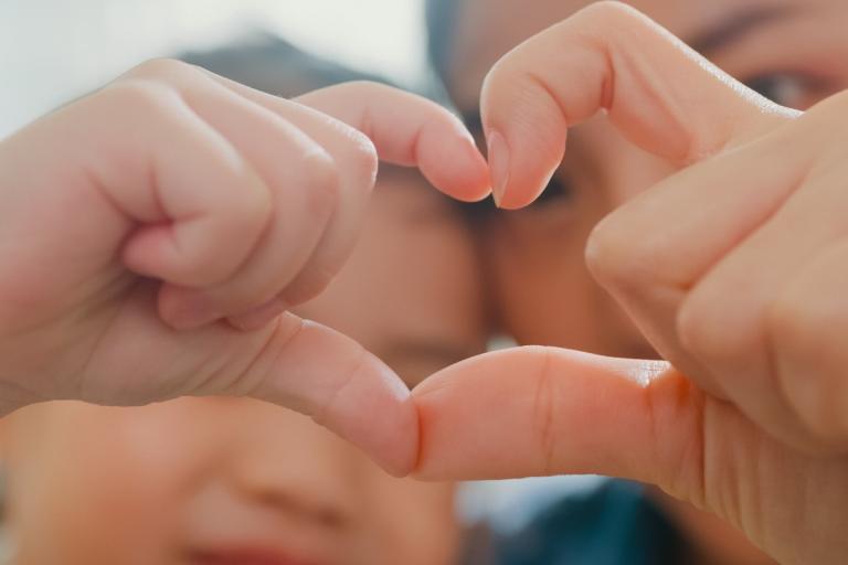 a child and an adult forming a heart shape by pressing together their fingers